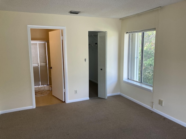 unfurnished bedroom featuring light colored carpet, a closet, a textured ceiling, and ensuite bathroom