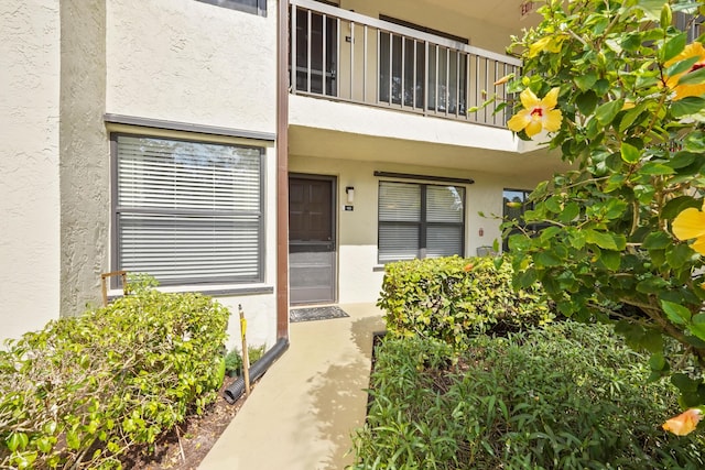 view of exterior entry featuring a balcony and stucco siding