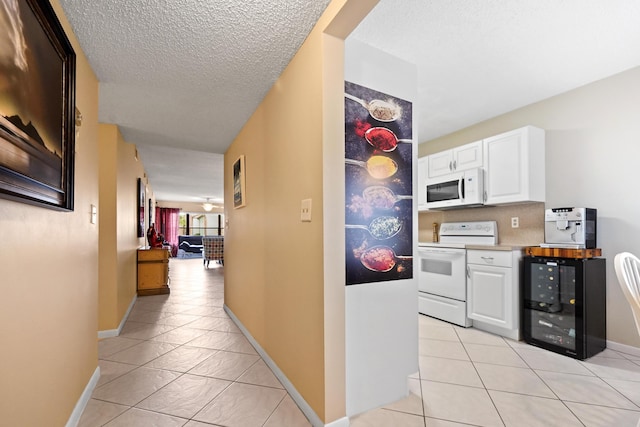 hallway with light tile patterned floors, wine cooler, a textured ceiling, and baseboards