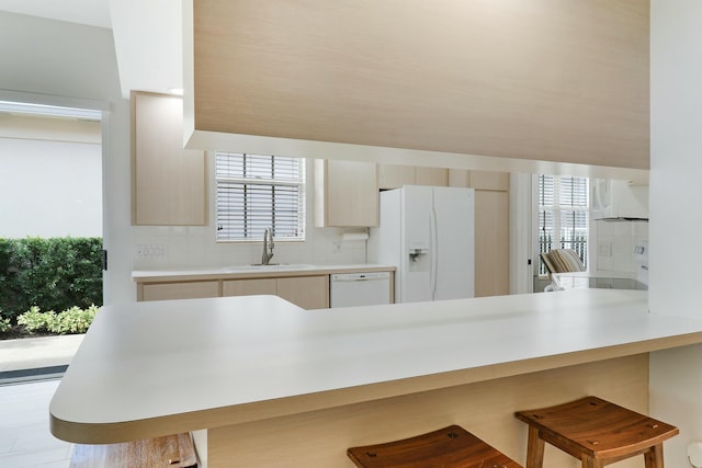 kitchen featuring sink, white appliances, backsplash, a kitchen breakfast bar, and kitchen peninsula