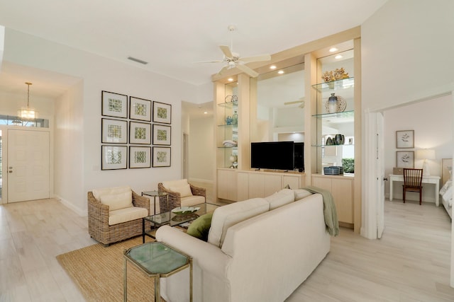 living room featuring a towering ceiling, built in features, light hardwood / wood-style floors, and ceiling fan