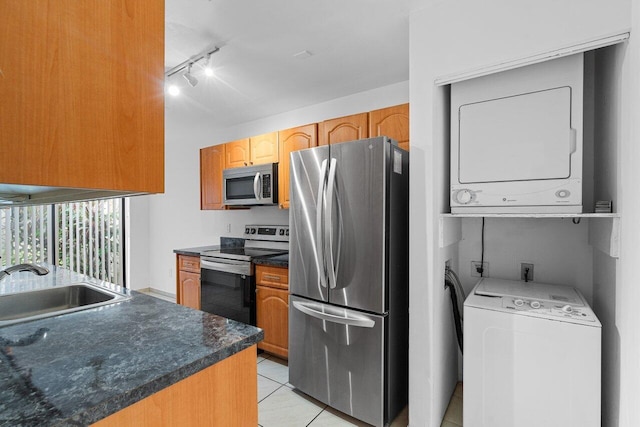 kitchen featuring stainless steel appliances, stacked washer and clothes dryer, sink, and light tile patterned floors