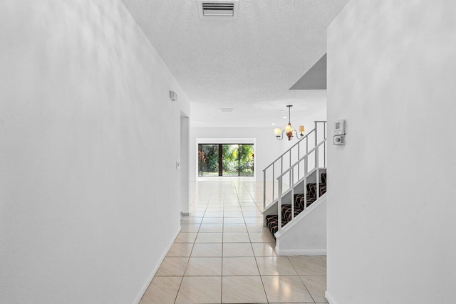 corridor with light tile patterned floors, a notable chandelier, and a textured ceiling