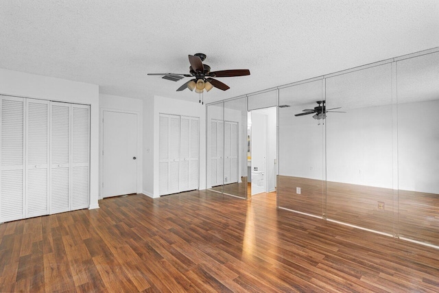 unfurnished bedroom with dark wood-type flooring, ceiling fan, multiple closets, and a textured ceiling