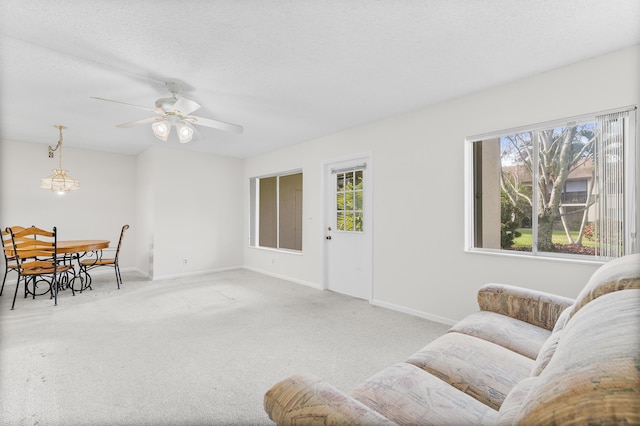 living room featuring plenty of natural light, ceiling fan with notable chandelier, light carpet, and a textured ceiling