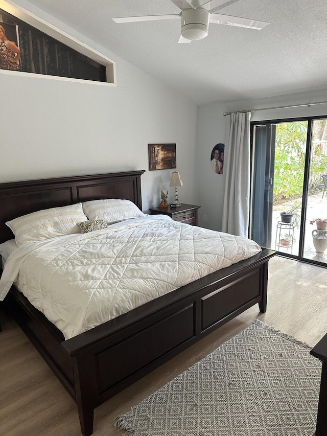 bedroom featuring hardwood / wood-style floors, lofted ceiling, access to outside, ceiling fan, and a textured ceiling