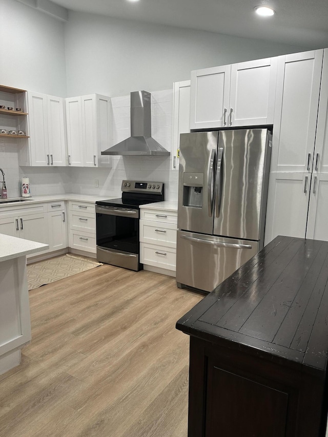 kitchen featuring wall chimney exhaust hood, lofted ceiling, light wood-type flooring, appliances with stainless steel finishes, and white cabinets