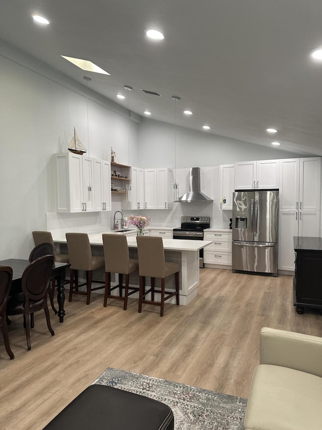 kitchen featuring white cabinetry, stainless steel appliances, a breakfast bar, and wall chimney exhaust hood