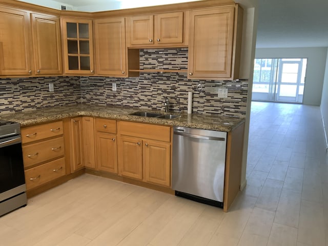 kitchen featuring sink, dark stone countertops, stainless steel appliances, tasteful backsplash, and light hardwood / wood-style floors