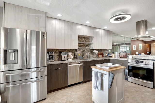 kitchen featuring sink, appliances with stainless steel finishes, tasteful backsplash, light stone countertops, and island exhaust hood