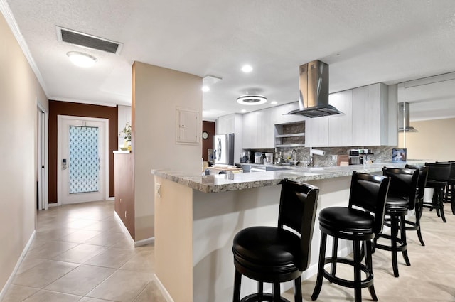 kitchen featuring light tile patterned floors, a breakfast bar area, island exhaust hood, stainless steel fridge with ice dispenser, and kitchen peninsula