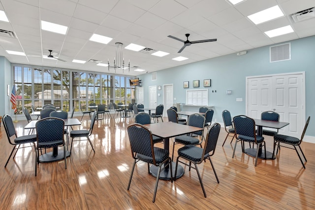 dining area featuring ceiling fan with notable chandelier, a drop ceiling, light hardwood / wood-style floors, and a wall of windows