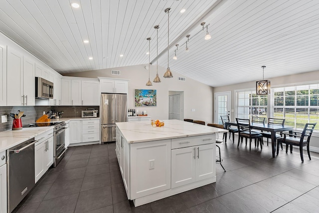 kitchen featuring white cabinetry, decorative light fixtures, appliances with stainless steel finishes, a kitchen island, and light stone countertops