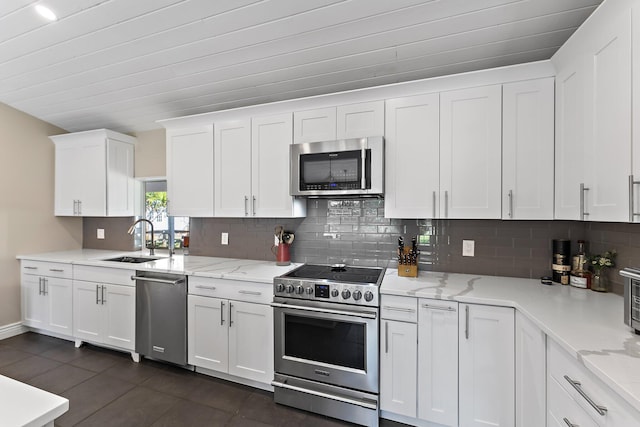 kitchen with sink, white cabinets, backsplash, light stone counters, and stainless steel appliances