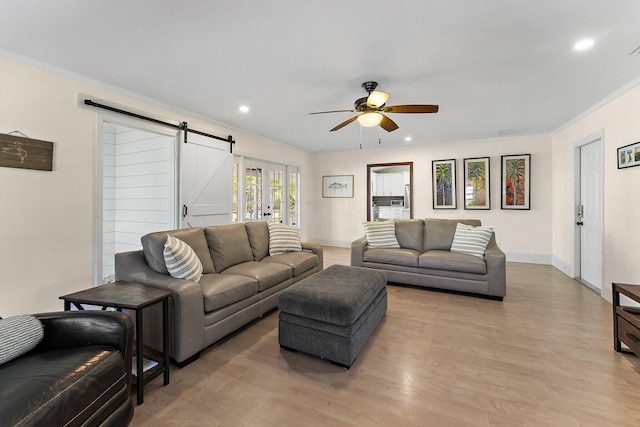 living room featuring ceiling fan, ornamental molding, a barn door, and light hardwood / wood-style floors