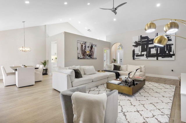 living room with ceiling fan with notable chandelier, high vaulted ceiling, and light hardwood / wood-style floors