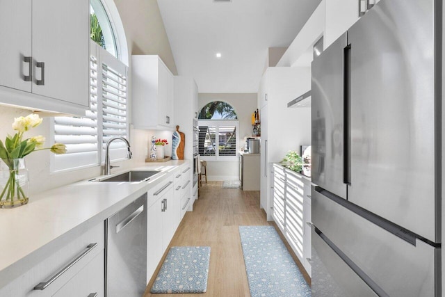 kitchen with sink, light hardwood / wood-style flooring, appliances with stainless steel finishes, white cabinets, and vaulted ceiling