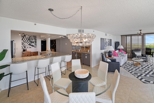 tiled dining room with sink, ceiling fan with notable chandelier, and a textured ceiling