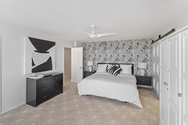 carpeted bedroom featuring ceiling fan, a barn door, and a textured ceiling