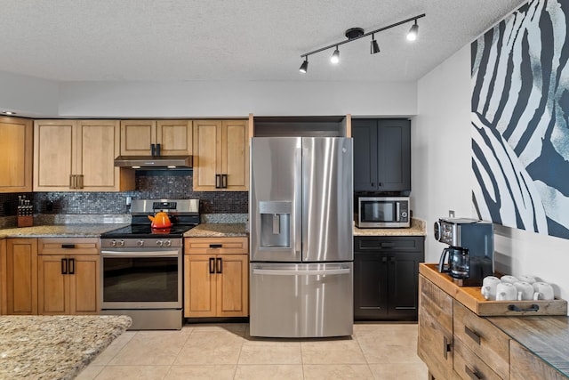 kitchen with light tile patterned floors, appliances with stainless steel finishes, tasteful backsplash, light stone countertops, and a textured ceiling