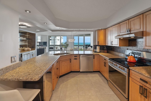 kitchen with sink, light stone counters, decorative light fixtures, kitchen peninsula, and stainless steel appliances