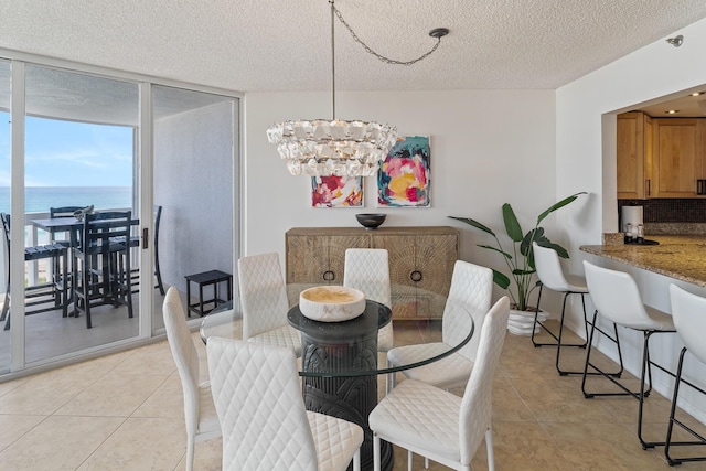 tiled dining area with floor to ceiling windows, a water view, a textured ceiling, and a chandelier