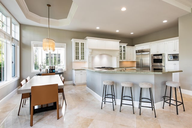 kitchen with white cabinetry, a spacious island, decorative light fixtures, built in appliances, and a kitchen bar