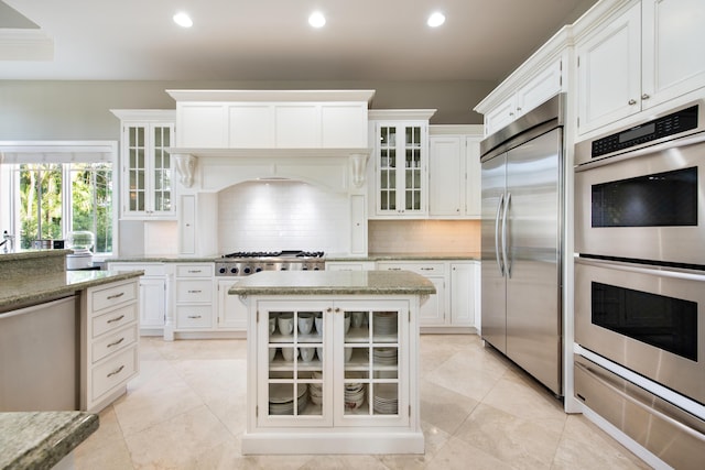 kitchen featuring a kitchen island, stainless steel appliances, white cabinets, light stone countertops, and decorative backsplash