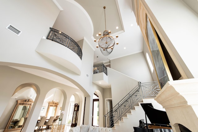 staircase with a notable chandelier, ornamental molding, and a towering ceiling