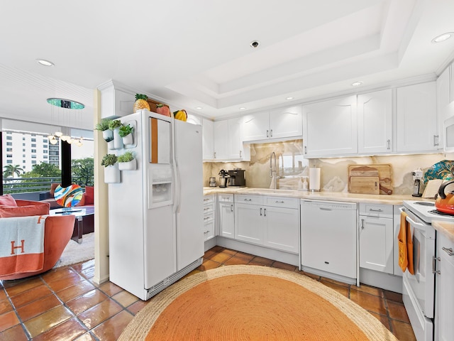 kitchen with a raised ceiling, white cabinetry, sink, and white appliances