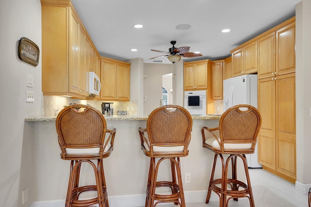 kitchen featuring white appliances, a kitchen bar, light brown cabinetry, and kitchen peninsula