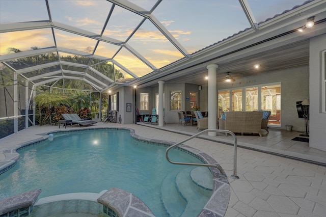 pool at dusk with outdoor lounge area, a patio, and glass enclosure