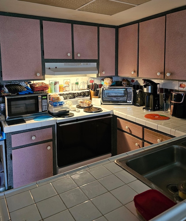 kitchen featuring a toaster, tile counters, under cabinet range hood, a sink, and range with electric stovetop