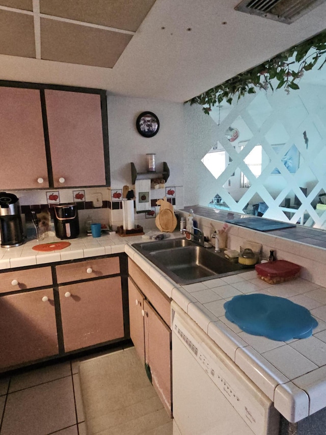 kitchen with tile countertops, light tile patterned flooring, white dishwasher, a sink, and visible vents