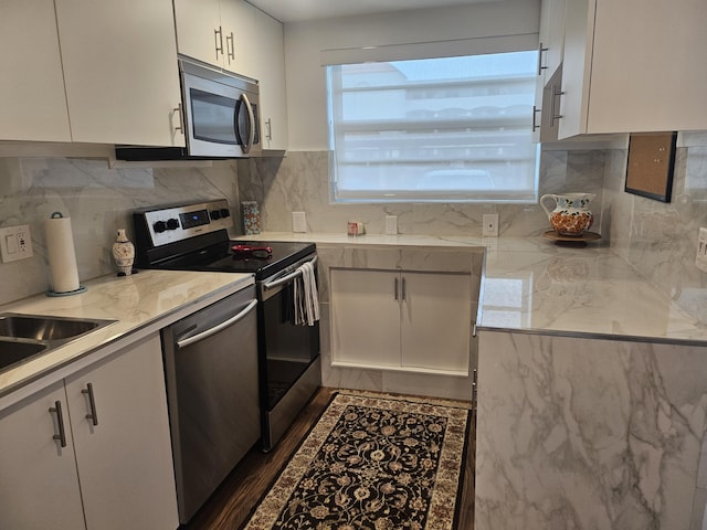 kitchen with sink, white cabinetry, light stone counters, appliances with stainless steel finishes, and backsplash