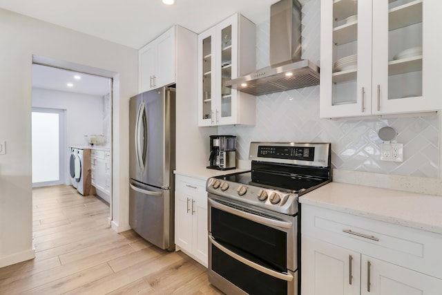 kitchen with washer / clothes dryer, decorative backsplash, white cabinets, appliances with stainless steel finishes, and wall chimney exhaust hood