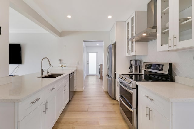 kitchen with a sink, stainless steel appliances, wall chimney exhaust hood, light wood-type flooring, and backsplash