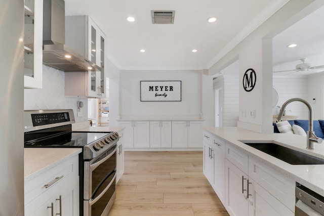 kitchen featuring a sink, light stone counters, stainless steel appliances, crown molding, and wall chimney range hood