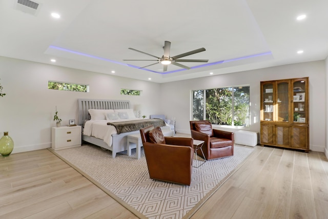 bedroom with visible vents, light wood finished floors, baseboards, a tray ceiling, and recessed lighting