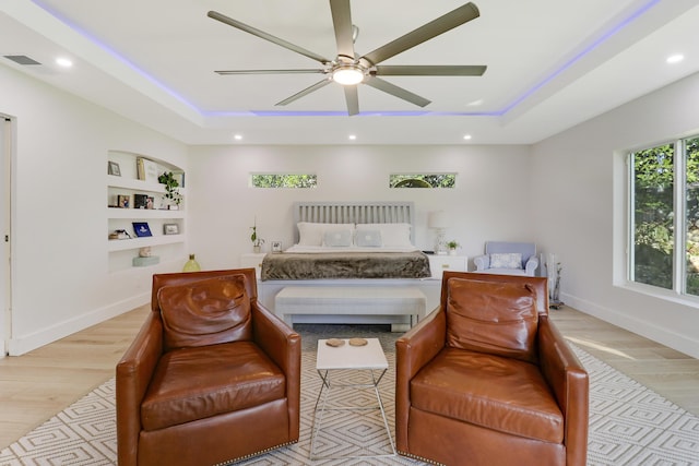 bedroom with a tray ceiling, light wood-style floors, and baseboards