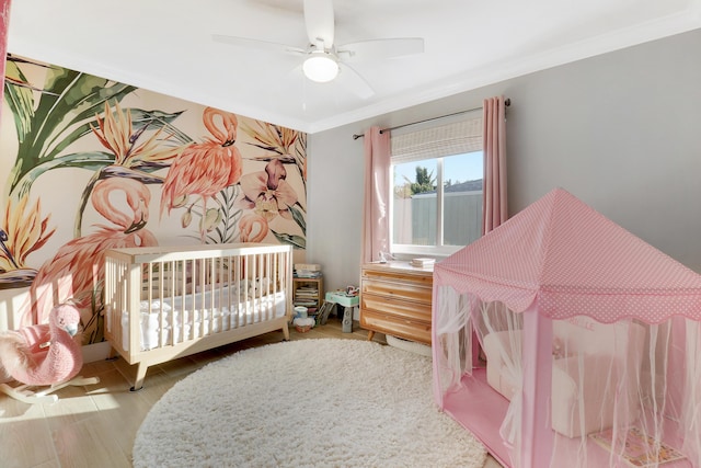 bedroom featuring wood finished floors, a nursery area, ceiling fan, and crown molding