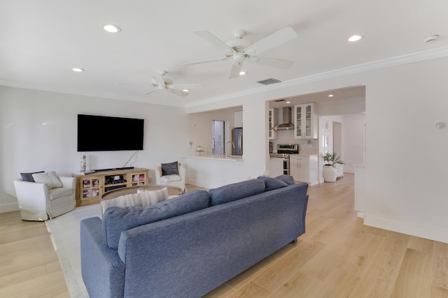 living room with light wood-type flooring, visible vents, baseboards, and crown molding