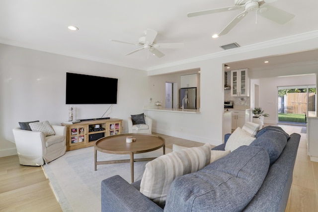 living room with visible vents, light wood-style flooring, a ceiling fan, and ornamental molding