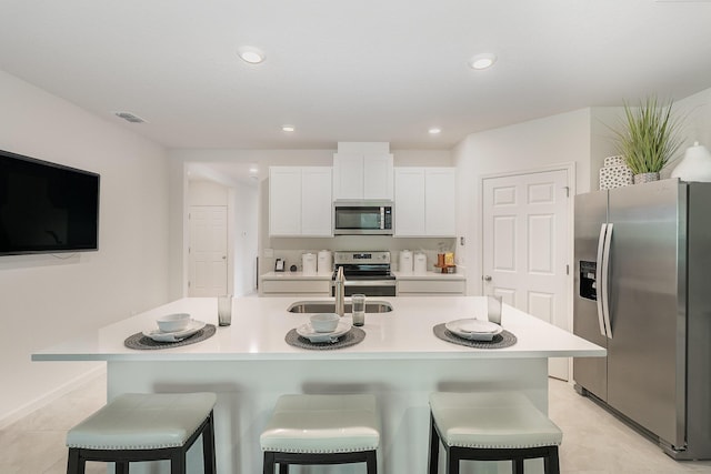 kitchen featuring white cabinetry, stainless steel appliances, a kitchen breakfast bar, and a center island with sink