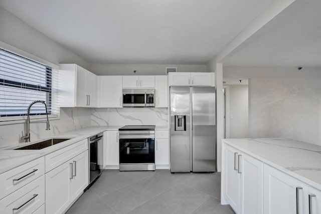 kitchen with sink, white cabinets, backsplash, stainless steel appliances, and light stone countertops