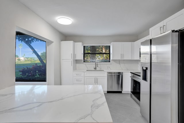 kitchen with sink, appliances with stainless steel finishes, light stone countertops, white cabinets, and decorative backsplash