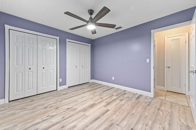 unfurnished bedroom featuring multiple closets, ceiling fan, and light hardwood / wood-style floors