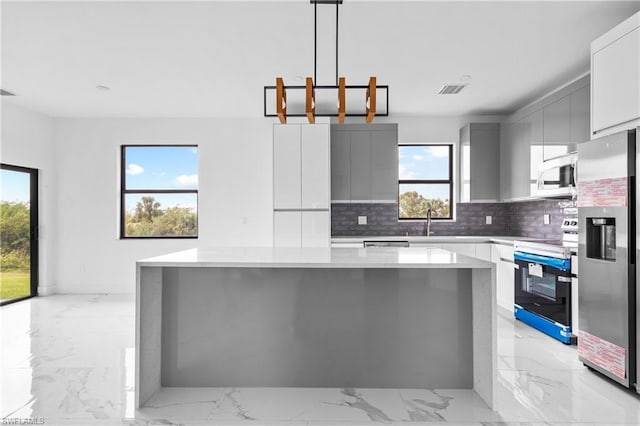 kitchen featuring pendant lighting, stainless steel appliances, light countertops, a kitchen island, and modern cabinets