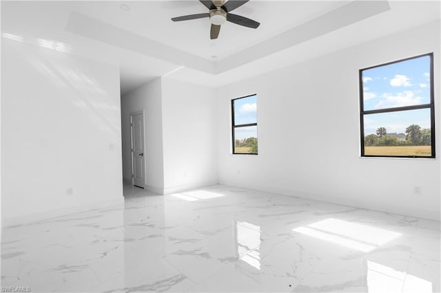 empty room with marble finish floor, ceiling fan, baseboards, and a raised ceiling