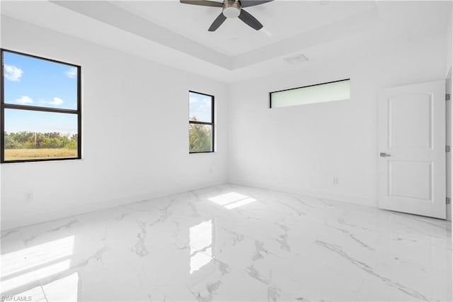 empty room with marble finish floor, a raised ceiling, visible vents, ceiling fan, and baseboards